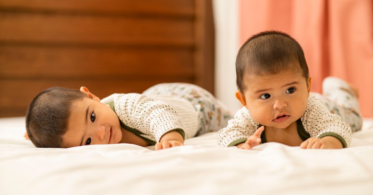 Adorable twin babies lying on a bed indoors, showcasing sibling love and bonding in a cozy setting.